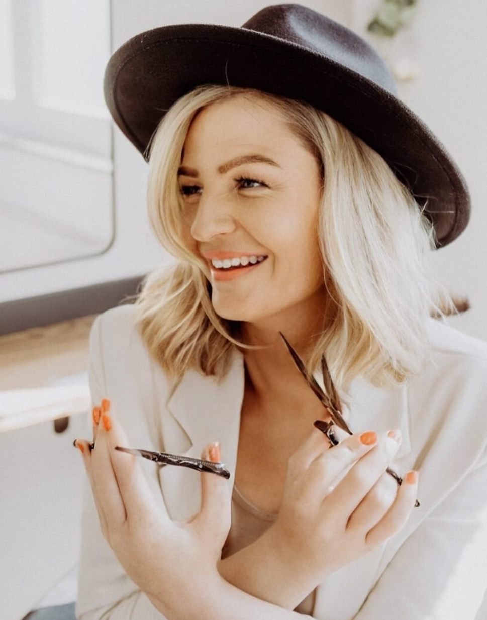 Nadine Rohm mit Hut, lächelnd, mit Friseurscheren in den Händen.